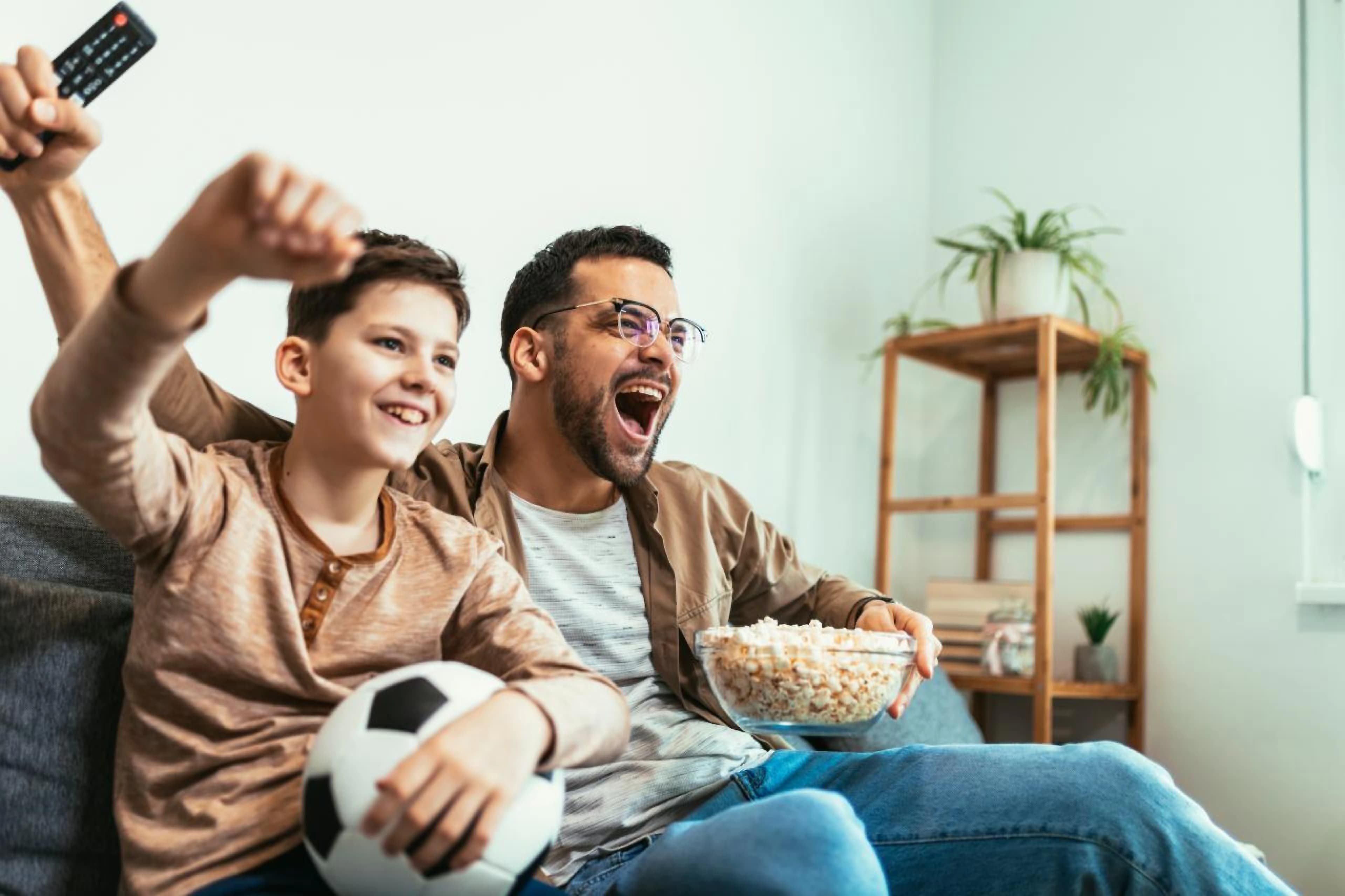 A father and child cheering while watching television